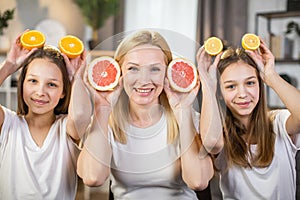 Mother with two daughters holding slices of citrus in hands