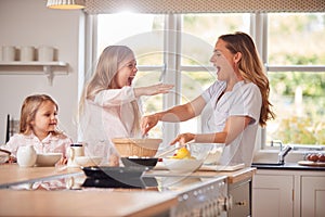 Mother And Two Daughters Making Pancakes In Kitchen At Home Together