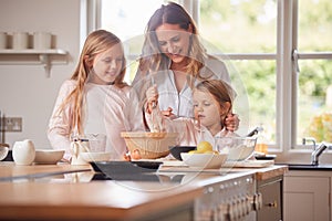 Mother And Two Daughters Making Pancakes In Kitchen At Home Together