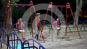 Mother and two daughters at playground enjoying at night in open air. Girls swing in the open air at night