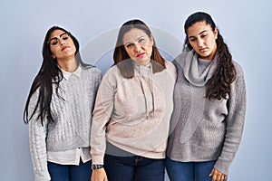 Mother and two daughters standing over blue background looking sleepy and tired, exhausted for fatigue and hangover, lazy eyes in
