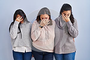 Mother and two daughters standing over blue background tired rubbing nose and eyes feeling fatigue and headache