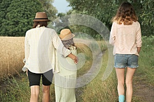 Mother and two daughters walking together along country road, back view