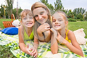 Mother and two girls lying on grass on a picnic and fun look into the frame