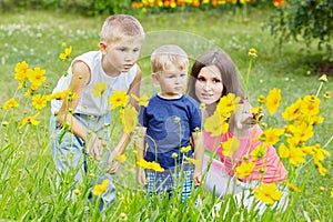 Mother and two her sons examine flower on lawn in photo