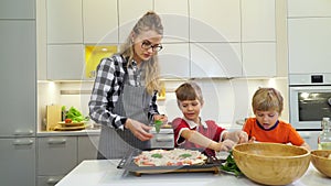 Mother and two kids making pizza with basil