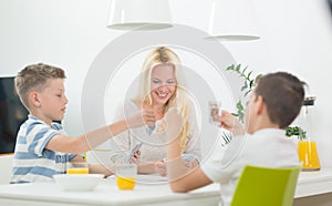 Mother and two kids playing card game at dining table at bright modern home.