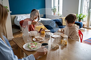 Mother and two kids sitting at kitchen table at home eating healthy food together in morning