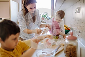 Mother of two little children preparing breakfast in kitchen at home.