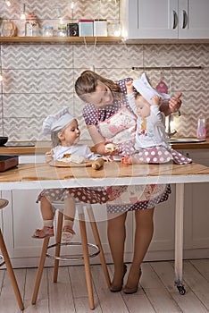 Mother and little daughters in cook hats cooking in the kitchen