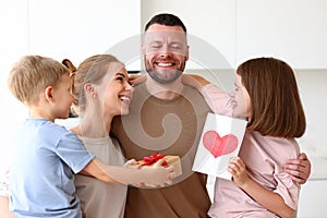 Mother and two smiling kids congratulating dad with Fathers day while standing in kitchen in morning