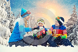 Mother and two sons drink hot tea in a snowy forest after sledging. Drink hot tea together.Family Winter fun for Christmas vacatio