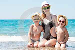 Mother and two sons in hats sitting on the beach.Summer family vacation.