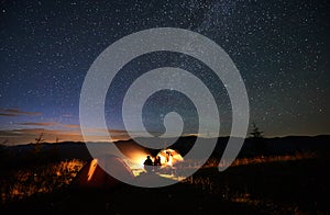 Mother and two sons hikers at camping in mountains under night sky full of stars and Milky way