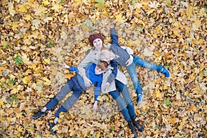 Mother and two sons lying on autumn foliage in forest. Young family in Park. Top view