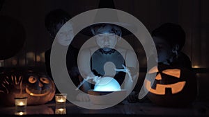 Mother with two sons playing a witch on Halloween. With a magic lamp and a pumpkin on the table at night.