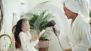 Mother use hair dryer with daughter, have fun in bathroom Spbd. Crazy cheerful family dance and sing