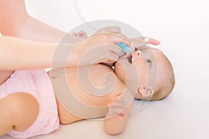 Mother using baby nasal aspirator. She is doing a mucus suction to four months baby girl photo