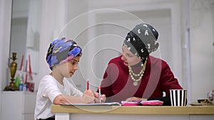 Mother using a laptop while assisting her daughter with schoolwork at home. Mother and little daughter doing homework