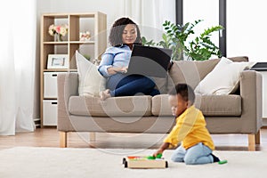 Mother using laptop and baby playing toy blocks