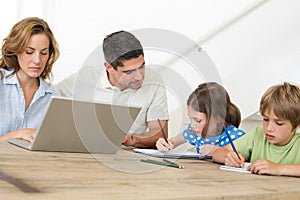 Mother using laptop while father assisting children in coloring