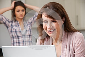 Mother Using Laptop With Frustrated Daughter In Background