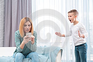 Mother using mobile phone while her son screaming and asking for attention. Lonely despaired child