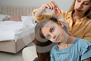 Mother using nit comb on her daughter`s hair in bedroom