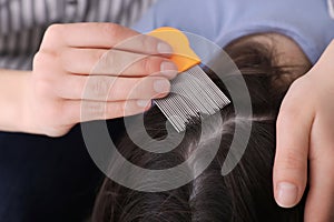 Mother using nit comb on her daughter`s hair indoors. Anti lice treatment photo