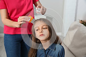 Mother using nit comb and spray on daughter`s hair at home. Anti lice