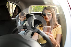 Mother using phone while driving car with her son on backseat