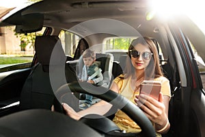 Mother using phone while driving car with her son on backseat