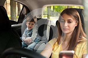 Mother using phone while driving car with her son on backseat