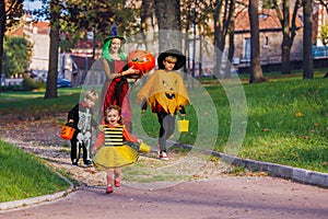 Mother walk with kids in Halloween costumes hold candies bucket