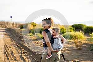 Mother walking while carrying a baby on her back in a baby carrier outdoors