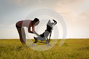 Mother walking her baby in stroller, outside at a beautiful park during sunset