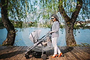 Mother walking her child near lake in city park with a beautiful pram