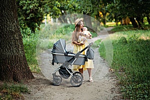 Mother walking with Newborn baby in Bassinet stroller in summer park in sunny day. Strollers for Newborns. Keep baby