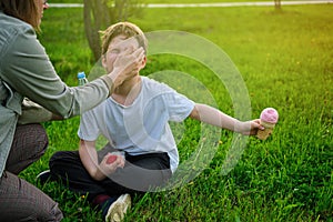 A mother washes the face of a boy soiled in ice cream on a park lawn