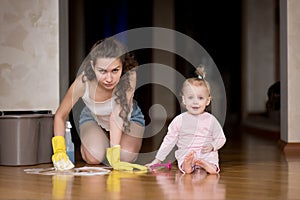 Mother is washing the floor, and the child is sitting nearby