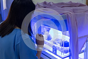 Mother watching at the Newborn baby with hyperbilirubinemia / Neonatal jaundice under blue UV light for phototheraphy on infant