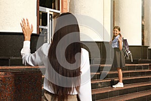 Mother waving goodbye to daughter near school entrance