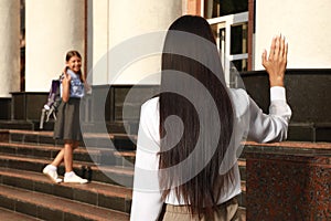 Mother waving goodbye to her daughter near school entrance