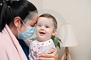 Mother wearing surgical or medical mask hugging cute baby girl