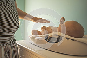 Mother weighs her newborn baby at home scales