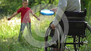 Mother in a wheel chair playing frisbee with son outdoors.