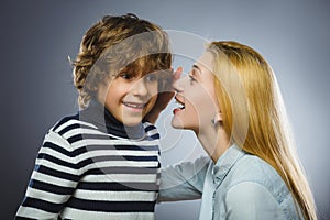 Mother whispering to son close up on gray background