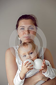 mother in white clothes holds her daughter in her arms at home