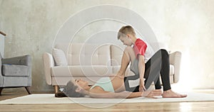 Mother woman doing glutei bridge workout exercise with son on her as dumbbell.