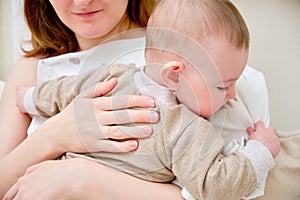 A mother woman holds an infant baby to regurgitate excess air after breastfeeding. Mom with a child boy holds vertically after